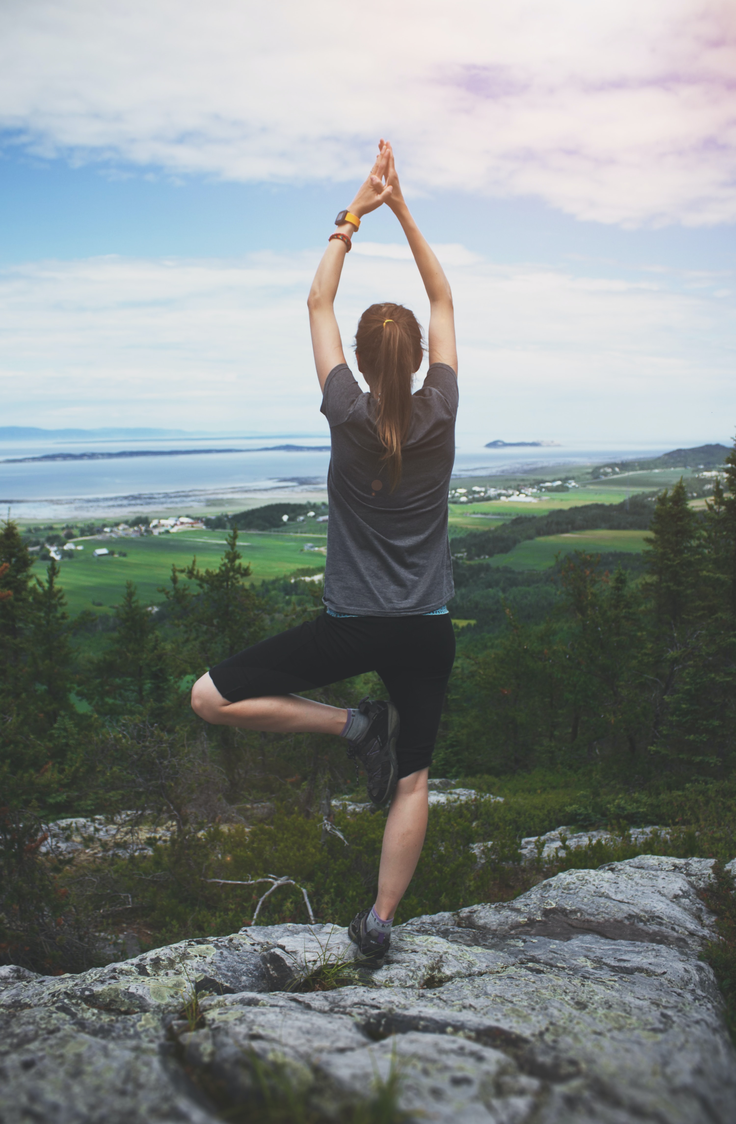 Woman standing on one leg at the top of a mountain in Kamouraska Title: Woman Standing on Mountain Top